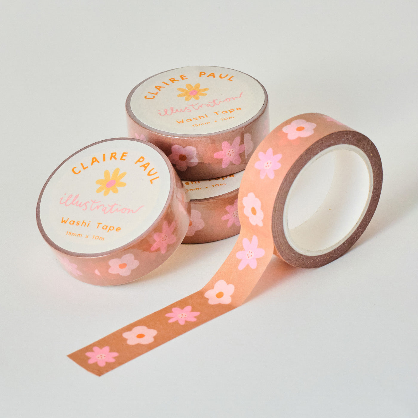 Stack of Brown Floral washi tapes in their packaging with an open roll. Tapes feature pattern of sweet pink flowers on a brown background. Each roll measures 15mm wide and has 10m of tape. Made by Claire Paul. 