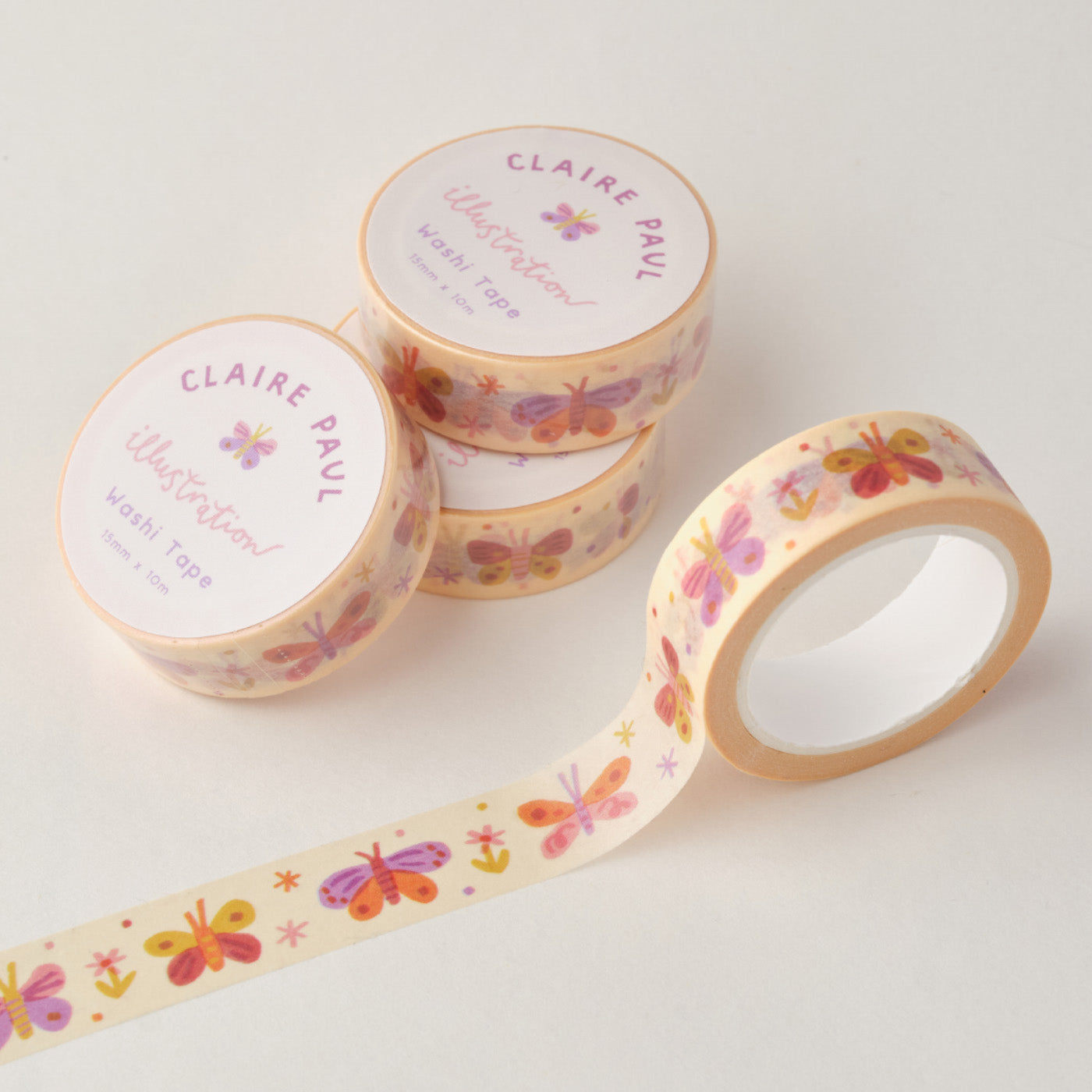 Stack of Pastel Butterfly washi tapes in their packaging with an open roll. Tapes feature pattern of hand drawn butterflies on a soft, cream background. Each roll measures 15mm wide and has 10m of tape. Made by Claire Paul. 