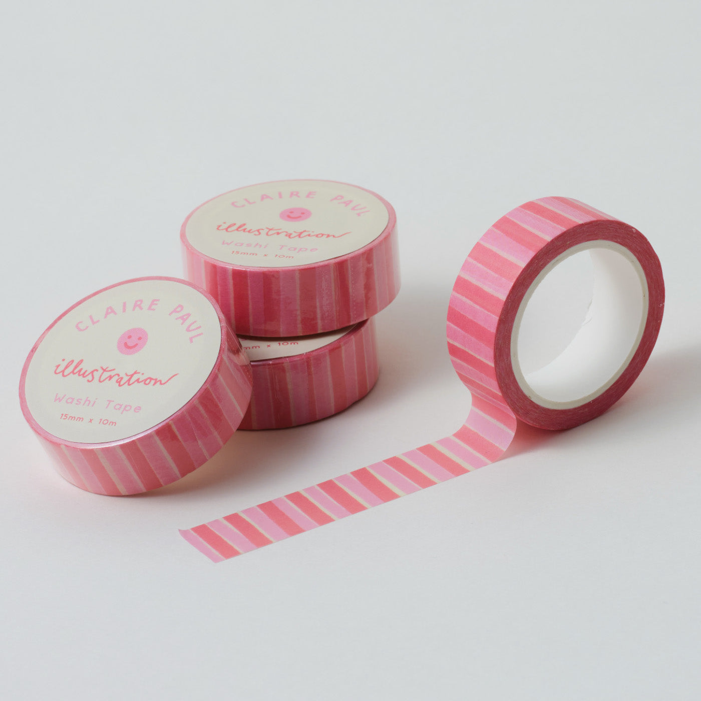 Stack of Pink Stripe washi tapes in their packaging with an open roll. Tapes feature pattern of vibrant pink stripes. Each roll measures 15mm wide and has 10m of tape. Made by Claire Paul. 