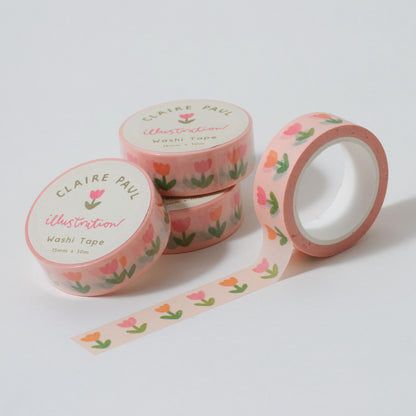 Stack of Tulip washi tapes in their packaging with an open roll. Tapes feature pattern of flowers on a pale pink background. Each roll measures 15mm wide and has 10m of tape. Made by Claire Paul. 