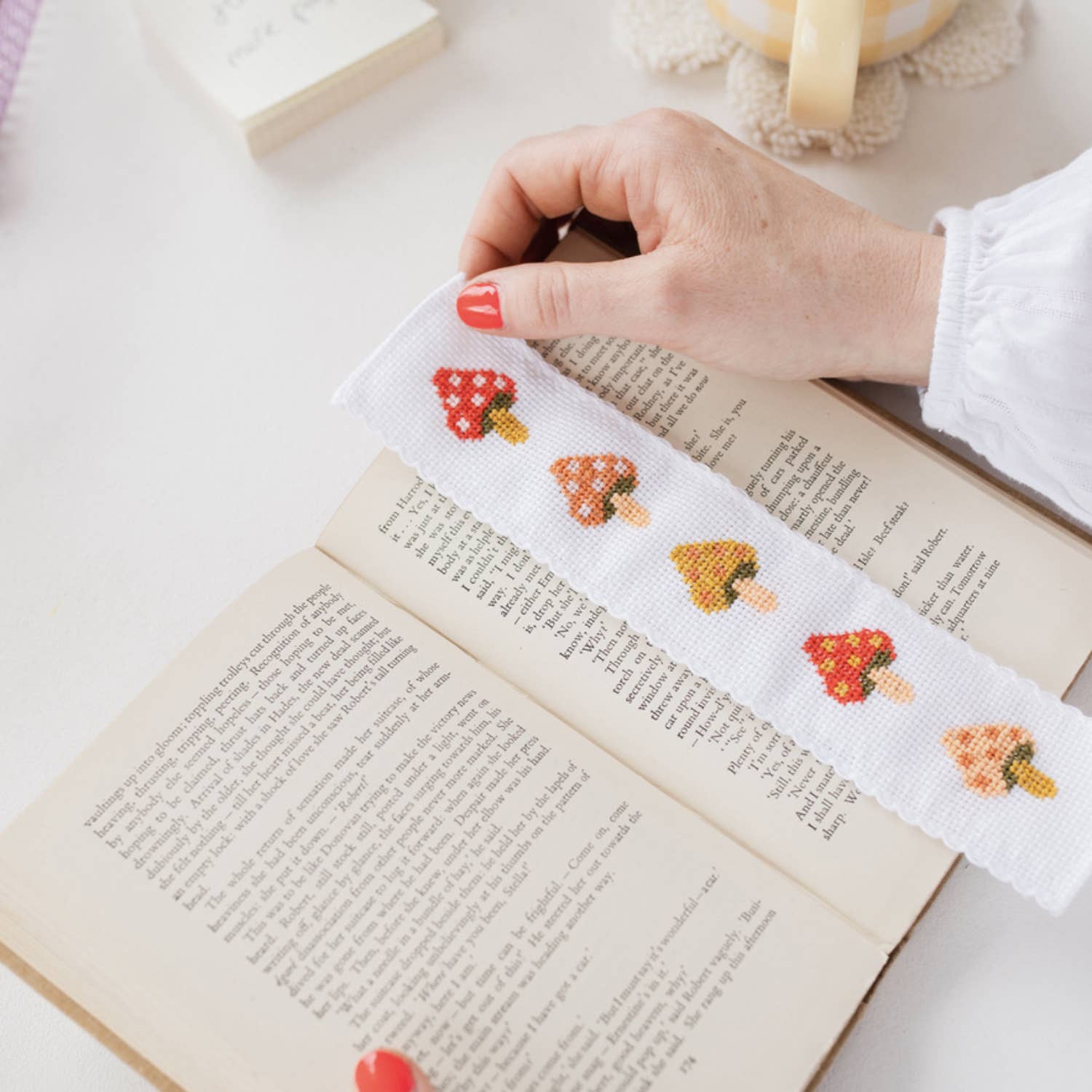 A finished cross-stitched mushroom patterned bookmark marking a place in a book.