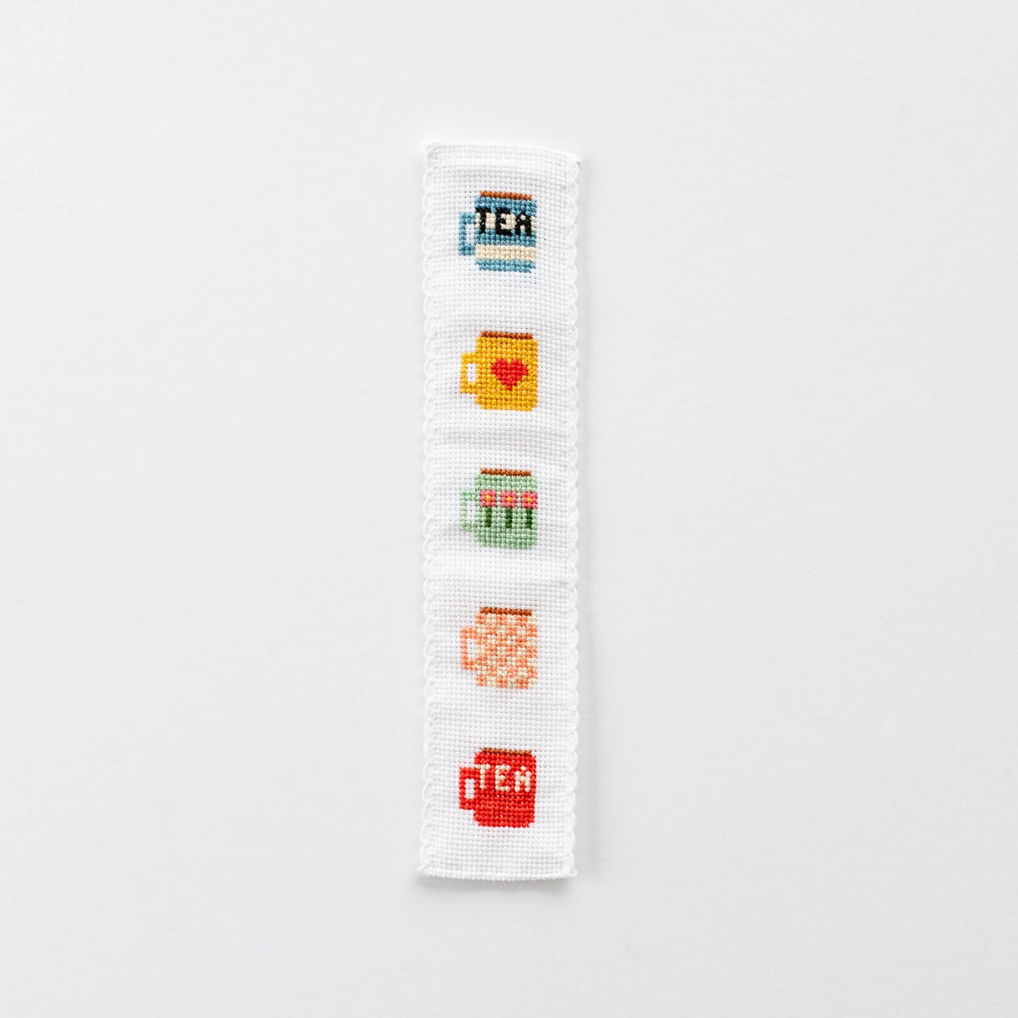 A finished cross-stitched bookmark with five tea mug motifs in bright colours.