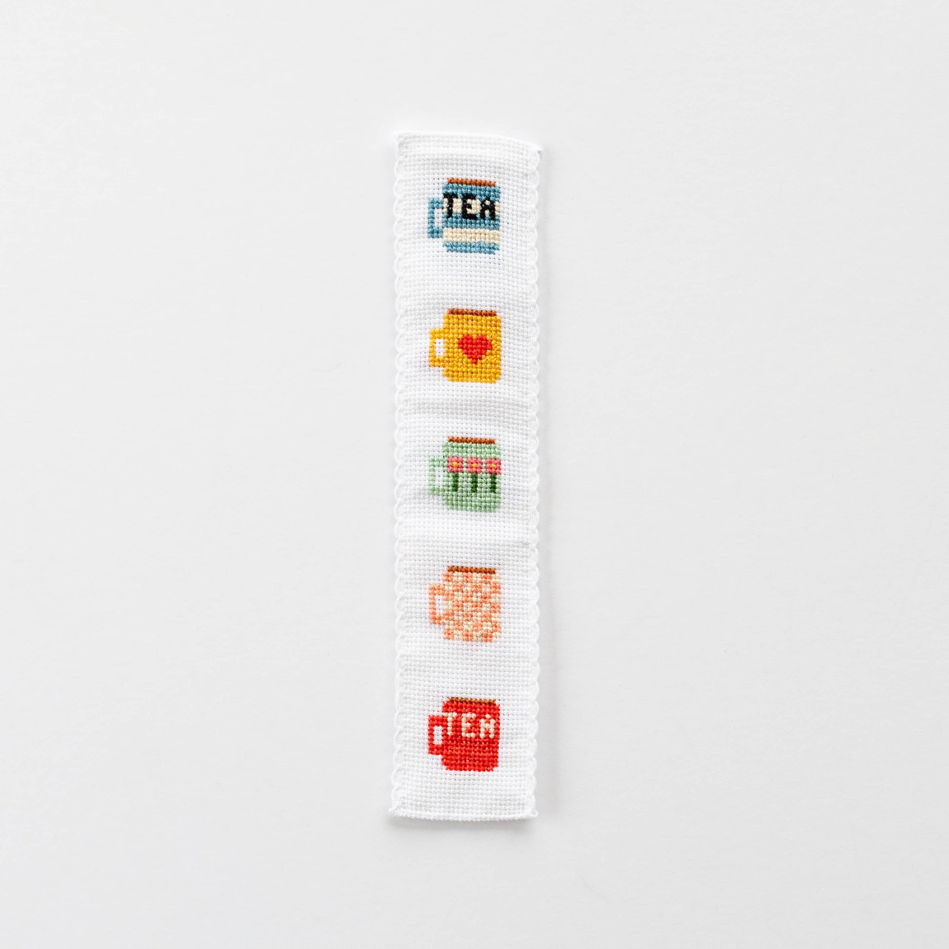 A finished cross-stitched bookmark with five tea mug motifs in bright colours.