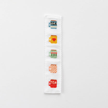 A finished cross-stitched bookmark with five tea mug motifs in bright colours.