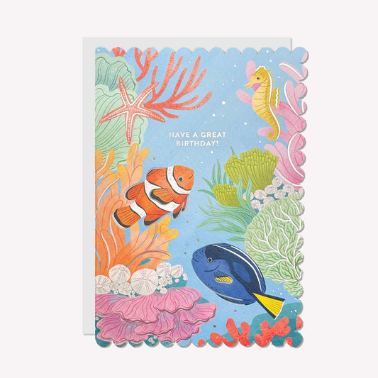 An illustrated birthday card by Raven Paper Co, printed by Ricicle Cards. This card features an underwater scene including clownfish and seahorse, with silver-foiled text above that reads “Have A Great Birthday!".