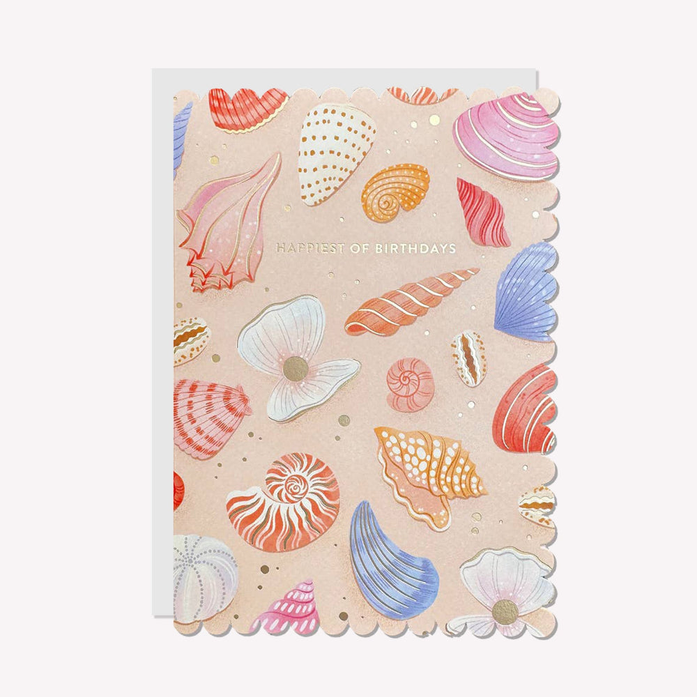 An illustrated birthday card by Raven Paper Co, printed by Ricicle Cards. This card features a pattern of sea shells with silver-foiled text above that reads “Happiest of Birthdays".