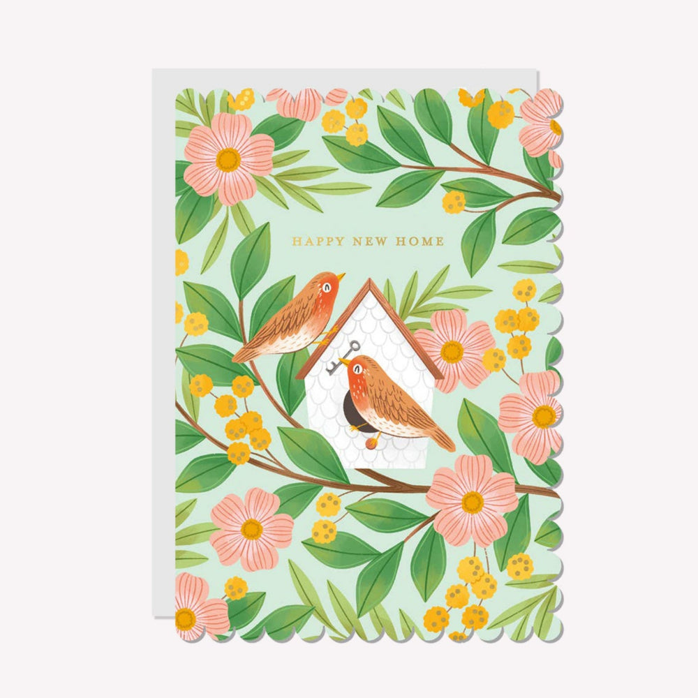 An illustrated new home card by Raven Paper Co, printed by Ricicle Cards. This card features an illustration of two birds at a nest box, with gold-foiled text above that reads “Happy New Home".