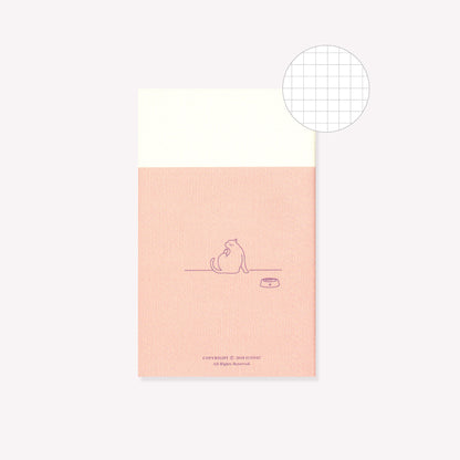 The back of the pink 'Yoga' design notebook by Iconic featuring a cat with their food bowl. A circular graphic indicates gridded pages inside.