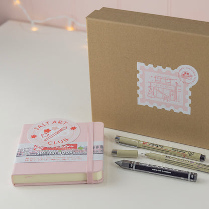 Salt Art Supply "Start a Sketchbook" creative Christmas Gift Box including a pink sketchbook, three drawing tools and a Salt Art Club sticker. 